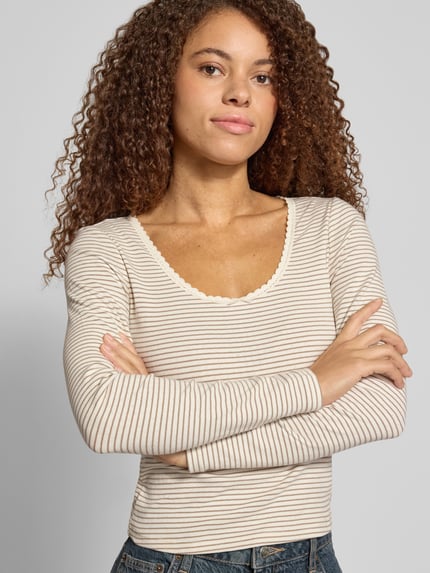 Frauenmodel trägt Slim Fit Langarmshirt aus Baumwoll-Mix von Levi's® 300, beige mit feinen braunen Streifen, Nahaufnahme Oberkörper.