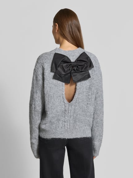 Vrouwenmodel draagt gebreide pullover Regular Fit Strickpullover aus elastischem Woll-Mix van Apricot, wolmix, ronde hals, ribboorden, ruglengte maat S 55 cm, mouwlengte maat S 68 cm, grijs met zwarte strikdetail, rugdecolleté, volledige achteraanzicht.