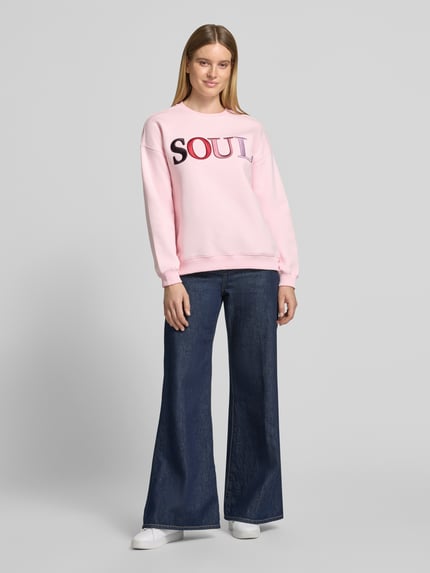 Frauenmodel trägt Oversized Sweatshirt aus Baumwoll-Mix mit Statement-Stickerei von Smith and Soul in Hellrosa, lange Ärmel, Rundhalsausschnitt, gerippte Abschlüsse, kastige Form, Ganzkörperansicht von vorne.