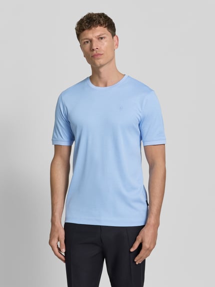 Mężczyzna nosi T-Shirt mit Rundhalsausschnitt od bugatti w jasnoniebieskim kolorze, bawełniany krój regular fit, detal z logo, widok całej sylwetki z przodu.