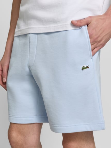 Männermodel trägt hellblaue Relaxed Fit Sweatshorts aus Baumwoll-Mix von Lacoste, glatte Oberfläche, Nahaufnahme Oberkörper, Herren Sweatshorts von Lacoste.