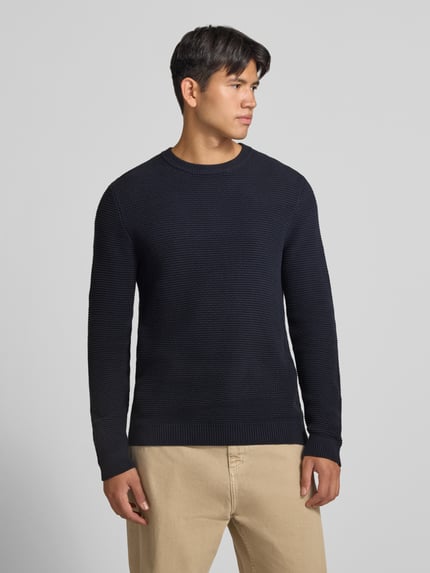 Männermodel trägt Regular Fit Strickpullover aus reiner Baumwolle von REVIEW, dunkle Farbe, strukturierte Oberfläche, Ganzkörperansicht von vorne, Rückenlänge 67 cm, Ärmellänge 72 cm, gerippte Abschlüsse und Blende