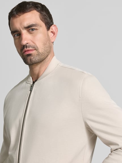 Männermodel trägt Jacke aus Viskose-Mix von MCNEAL in Beige mit Stehkragen und Reißverschluss, Nahaufnahme Oberkörper, gerader Schnitt. Rückenlänge 66 cm, Schulterbreite 45 cm, Brustweite 52 cm, Ärmellänge 68 cm, Stretch-Anteil, Eingrifftaschen.