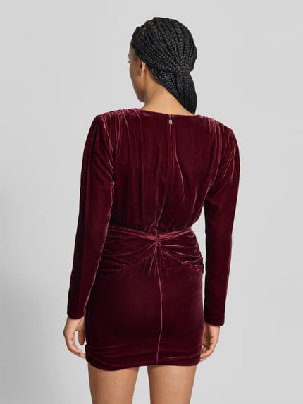 Vrouwenmodel draagt Minikleid aus Viskose-Mix van ROTATE in bordeauxrood fluweel, siergarnering, nauwsluitend model, met lange mouwen, totale lengte maat 36: 86 cm, borstwijdte: 44 cm, mouwlengte: 63 cm, rugaanzicht.