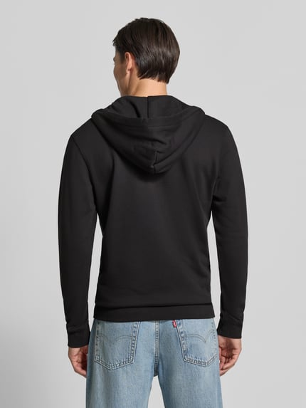 Männermodel trägt bluza rozpinana z bawełny o prostym kroju od Scotch & Soda, czarna, widoczne kaptur z trokiem, rękawy długie, wykończenia prążkowane, kieszeń kangurka i naszywka z logo, długość tyłu w rozmiarze M: 70 cm, długość rękawów: 68 cm, Ganzkörperansicht Rückansicht.