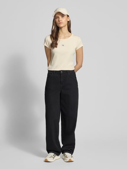 Frauenmodel trägt Cropped T-Shirt in Ripp-Optik mit Label-Badge von Calvin Klein Jeans, Baumwoll-Elasthan-Mix, Cremefarbe, Ganzkörperansicht von vorne.