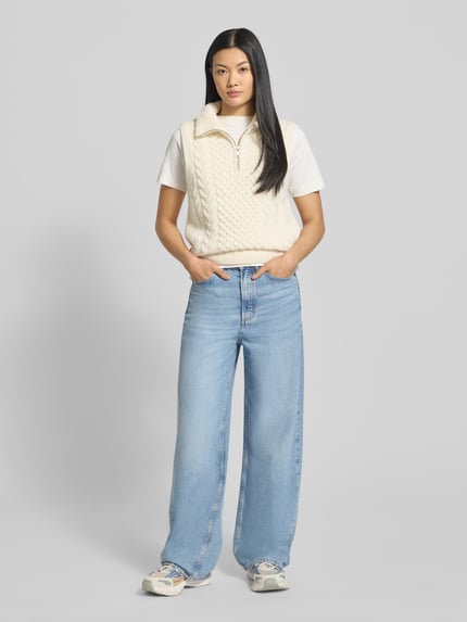Frauenmodel trägt Relaxed Fit Pullunder aus reinem Woll-Mix Modell 'OLAIAAS CABLE' von Armedangels, Optik:Unifarben, Struktur-Optik, Label-Patch, Troyer-Kragen, Passform: Relaxed-Fit, Materialverarbeitung: Strick, Farbe Creme, Ganzkörperansicht von vorne.