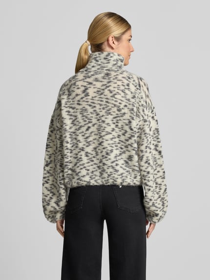 Frauenmodel trägt Oversized Turtleneck-Pullover aus Woll-Mix von ARMEDANGELS, cremefarben mit schwarzem Muster, lange Ärmel, Ganzkörperansicht Rückansicht. Damen Turtleneck-Pullover von ARMEDANGELS.