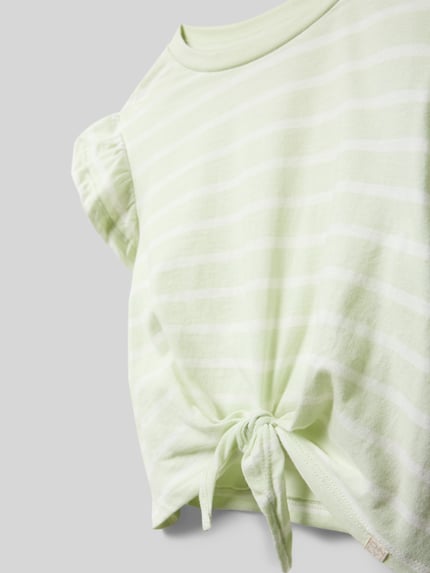Mädchen trägt Regular Fit T-Shirt aus reiner Baumwolle Modell 'KALINKA' von Only mit Allover-Muster, Knotendetail, Nahaufnahme Oberkörper.