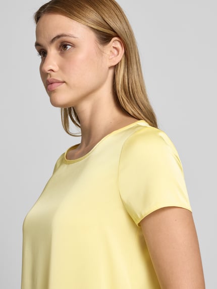 Kobiece modelka nosi Blusenshirt mit Rundhalsausschnitt und abgerundetem Saum von Rinascimento w jasnożółtym kolorze, materiał z domieszką stretchu, luźny krój, długość tyłu w rozmiarze S: 52 cm, zbliżenie na górną część ciała z przodu
