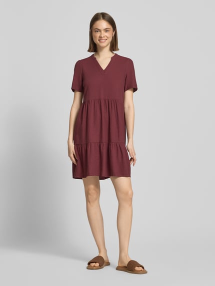 Vrouwenmodel draagt A-lijn vrijetijdsjurk uit mix van viscose en linnen model 'TIRI-GOA' van Only, look: effen, minilengte, v-hals, jurk met korte mouwen, materiaalverwerking: gevlamd garen, kleur bordeauxrood, gladde textuur, geheel lichaamsaanzicht van voren.