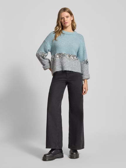 Frauenmodel trägt Relaxed Fit Strickpullover mit Woll-Anteil Modell 'MAINE' von Only in Two-Tone-Optik mit Paillettenbesatz, Rundhals, langarm, gerippte Abschlüsse, überschnittene Schultern, Strick-Materialverarbeitung, Ganzkörperansicht von vorne.