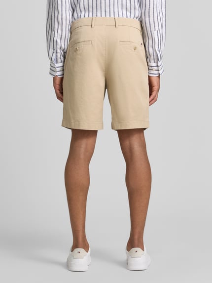 Męski model nosi Chinoshorts aus Baumwoll-Mix Modell 'DOVER' od Tommy Hilfiger, beżowy kolor, krój regular fit, widok całej sylwetki od tyłu.