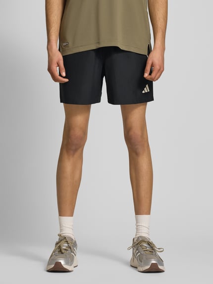 Męski model nosi Regular Fit Sport-Shorts mit Kontraststreifen von adidas Sportswear, efekt: jednolity kolor, krój regular fit, nadruk z logo, elastyczny ściągacz z tunelem, kieszenie zapinane na zamek błyskawiczny; Ganzkörperansicht von vorne.