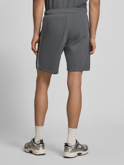 Männermodel trägt graue Shorts mit Logo und elastischem Bund von CHAMPION, Baumwoll-Mix, Regular Fit, Ganzkörperansicht Rückansicht.