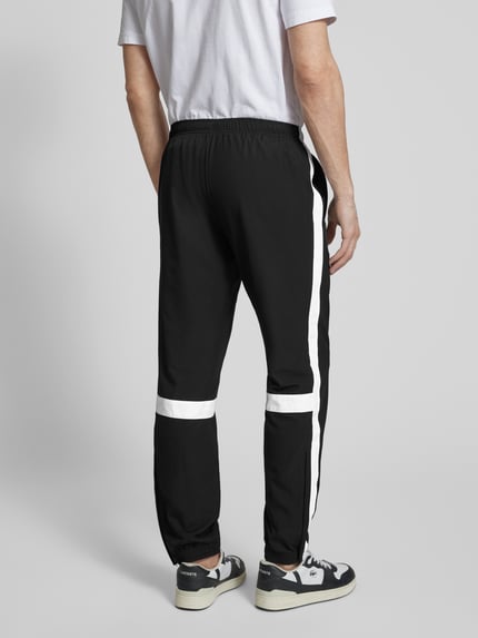 Männermodel trägt Regular Fit Trainingsanzug mit Kontraststreifen von Lacoste Sport in Schwarz mit weißen Streifen, Ganzkörperansicht Rückansicht.