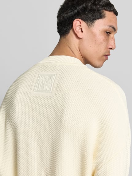 Männermodel trägt Strickjacke mit floralem Stitching von MAISON KITSUNÉ, kremowy, mieszanka bawełny, krój regular fit, detalaufnahme z tyłu.