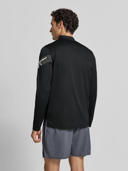 Męski model nosi bluzkę z długim rękawem Model 'ICON' od ASICS TIGER, czarna, prosty krój, nadruk z logo, kołnierz zapinany, Długość tyłu w rozmiarze M: 72 cm, widok całej sylwetki z tyłu.