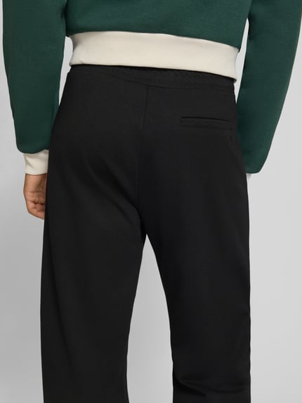 Männermodel trägt Straight Fit Sweatpants mit elastischem Bund von REVIEW in Schwarz, glatte Textur, Detailaufnahme Rückansicht.