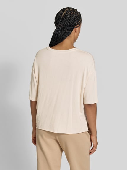 Kobiece model prezentuje T-Shirt mit U-Boot-Ausschnitt od Juvia w kolorze jasnego beżu z mieszanki bawełny i modalu, krój relaxed fit, dekolt w łódkę, luźne ramiona, rękaw o dł. 1/2, długość tyłu w rozmiarze S: 55 cm, widok całych pleców