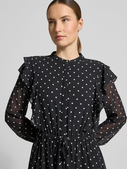 Frauenmodel trägt Midikleid im Allover-Look mit Bindegürtel von JOOP! in Schwarz mit weißen Punkten, Volants, Rundhalsausschnitt, Nahaufnahme Oberkörper. Rückenlänge bei Größe 36: 120 cm, Brustweite: 47 cm, Ärmellänge: 63 cm.