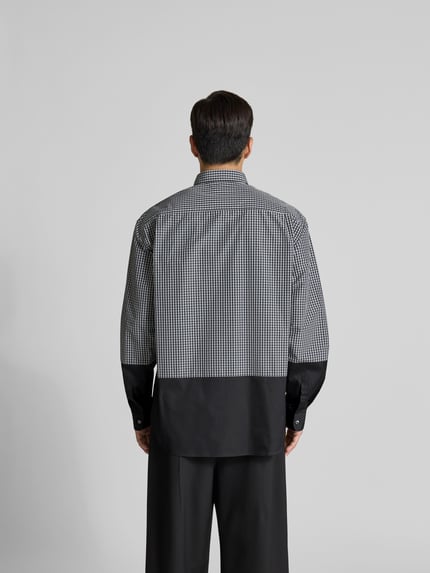 Męski model nosi Relaxed Fit Freizeithemd mit Brusttasche von VETEMENTS z mieszanki bawełny, czarno-biała krata, długość tyłu 85 cm, szerokość w rozmiarze M: 53 cm, długość rękawów 68 cm, krój z długim rękawem, listwa guzikowa na całej długości, brustasza z wyhaftowanym logo, widok całej sylwetki z tyłu.
