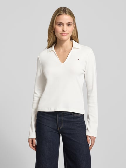 Frauenmodel trägt Slim Fit Langarmshirt aus reiner Baumwolle von Tommy Hilfiger in Unifarbe mit V-Ausschnitt und Logo-Detail, Ganzkörperansicht von vorne