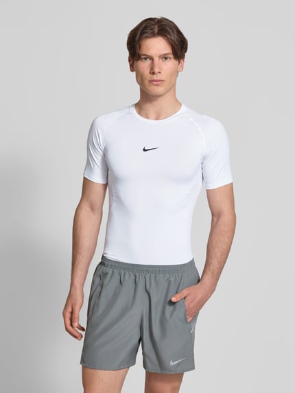 Männermodel trägt T-Shirt mit Logo-Print und Rundhalsausschnitt von NIKE TRAINING, Slim-Fit, Raglanärmel, weiße Farbe, Ganzkörperansicht von vorne. Rückenlänge bei Größe M: 72 cm.