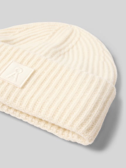 Produktfoto, cremeweiße Mütze aus reiner Wolle Modell 'ICONIC Å WOOL' von ARMEDANGELS, gerippte Struktur auf grauem Hintergrund