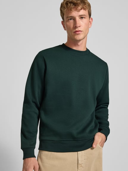 Männermodel trägt Regular Fit Sweatshirt mit Baumwoll-Anteil Modell 'Bradley' von JACK & JONES in Dunkelgrün, Nahaufnahme Oberkörper. Material-Mix, Rundhalsausschnitt, Langarm, gerippte Abschlüsse, Logo-Label.