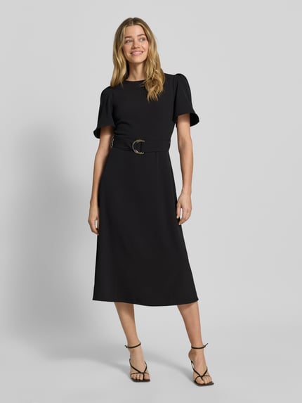 Frauenmodel trägt Cocktailkleid mit Gürtel und Rundhalsausschnitt von Rinascimento in Schwarz, Material-Mix mit Stretch-Anteil, Taillierter Schnitt, Midikleid, rückseitiger Reißverschluss, Rückenlänge 36 cm, Brustweite 40 cm, Ärmellänge 28 cm, Ganzkörperansicht von vorne.