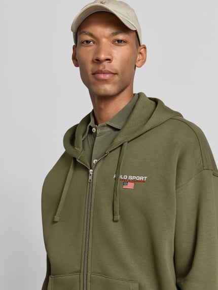 Männermodel trägt Regular Fit Sweatjacke aus Baumwoll-Mix von Polo Ralph Lauren in Olivgrün mit kleiner Logo-Stickerei, Nahaufnahme Oberkörper. Herren Sweatjacke von Polo Ralph Lauren