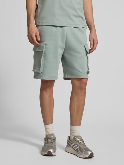 Männermodel trägt Sweatshorts mit Cargotaschen und Logo von CHAMPION in Mintgrün, Baumwoll-Mix, Relaxed Fit, Nahaufnahme Oberkörper bis Knie.