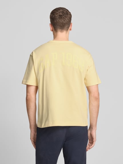 Männermodel trägt T-Shirt mit Logo und Rundhalsausschnitt von GAP in Gelb, Reine Baumwolle, Regular-Fit, Rückenlänge 61 cm, Ganzkörperansicht Rückansicht.