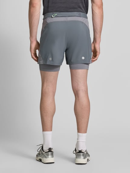 Männermodel trägt Regular Fit Shorts mit integrierten Tights Modell 'Road' von ASICS TIGER in Grau mit Logo-Detail, Ganzkörperansicht Rückansicht.