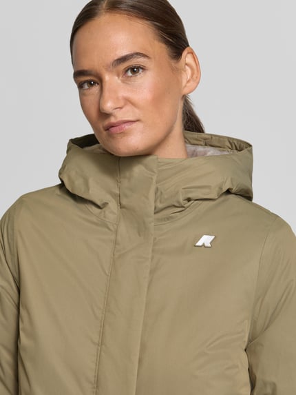 Frauenmodel trägt Regular Fit Mantel mit Logo-Applikation Modell 'SOPHIE' von K-WAY in Khaki mit Kapuze und Stehkragen, Nahaufnahme Oberkörper. Rückenlänge 73 cm, Schulterbreite 41 cm, Brustweite 46 cm, Ärmellänge 53 cm.