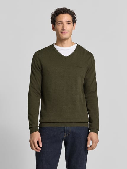 Männermodel trägt Pullover mit Logo-Detail von S.OLIVER CASUAL, unifarben, V-Ausschnitt, Feinstrick, gerippte Abschlüsse, Ganzkörperansicht von vorne.