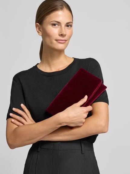 Vrouwenmodel draagt Clutch uit leer met ritsvak binnen van Abro in bordeauxrood, gladde textuur, Nahaufnahme bovenlichaam. Context: dames clutch van echt leer, hoofdvak met overslag en magneetsluiting, labeldetail binnenin, afmetingen 23x14x4 cm.