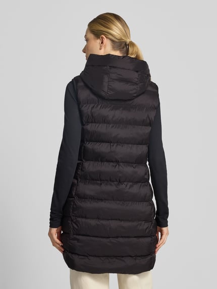 Vrouwenmodel draagt Regular Fit bodywarmer in stiksels van FUCHS SCHMITT, zwart met capuchon en steekzakken met ritssluiting, ruglengte 77 cm, schouderbreedte 41 cm, borstwijdte 51 cm, doorgestikte structuur, ganzebody van achteraanzicht.