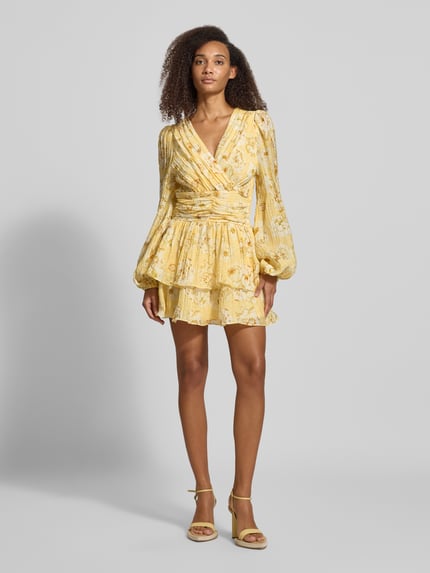 Modelka prezentuje Minikleid aus Viskose-Mix mit Rüschenbesatz von Gina Tricot, żółte wzory, krój taliowany, długi rękaw, rozkloszowana spódnica, dekolt V, dziewczęca tekstura, szerokość w rozmiarze 36: 41 cm, długość tyłu: 80 cm, długość rękawa: 69 cm, widok całej sylwetki z przodu.