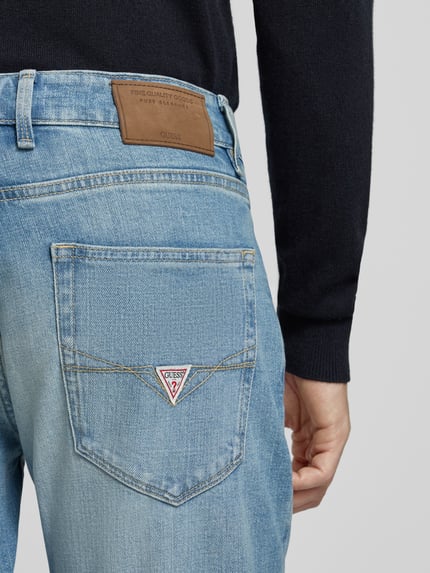 Mężczyznamodel nosi jeansy Slim Fit Jeans im Used-Look Model 'ANGELS' od GUESS, mieszanka bawełny i elastanu, wpuszczane kieszenie, efekt znoszenia, jasnoniebieski denim, naszywka GUESS z tyłu, Szerokość w rozmiarze 32/32: 43 cm, Długość wewnętrzna nogawki: 80 cm, Ganzkörperansicht Rückansicht