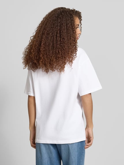 Modelka prezentuje damski t-shirt z bawełny, krój oversized, nadruk z motywem z tyłu, okrągły dekolt, REVIEW, widok całych pleców.