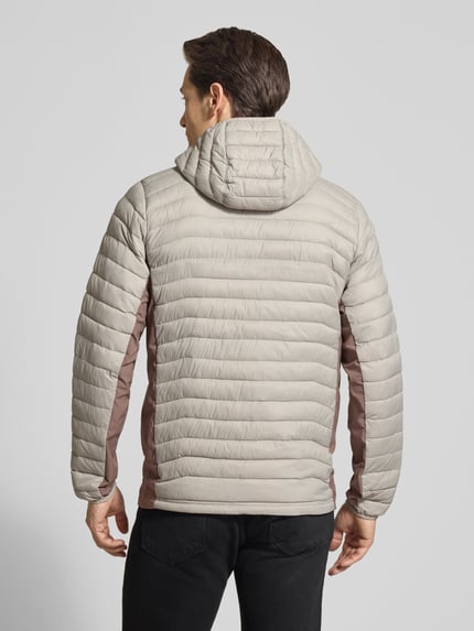 Männermodel trägt Steppjacke mit Kapuze und Logo von Columbia in Beige und Braun, Regular-Fit, Rückenlänge 72 cm, Ganzkörperansicht Rückansicht.