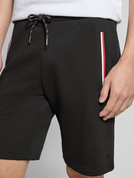 Männermodel trägt schwarze Shorts mit elastischem Bund von Christian Berg Men aus Baumwoll-Elasthan-Mix, Eingrifftaschen mit Kontraststreifen, Nahaufnahme Oberkörper. Regular-Fit, Bundweite in Größe M 43 cm, Innenbeinlänge 23 cm.