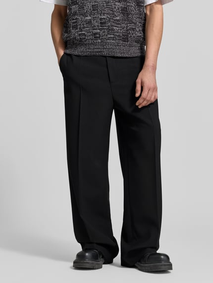 Männermodel trägt Relaxed Fit Stoffhose aus Woll-Mix von Filippa K in Schwarz mit Bundfalten, Eingriff- und Gesäßtaschen, Nahaufnahme Unterkörper.