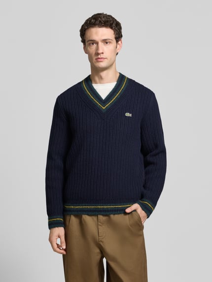 Männermodel trägt Pullover mit Logo-Patch aus Wolle Alpaka von LACOSTE in Strickoptik, dunkelblau mit grünen Details, Ganzkörperansicht von vorne.