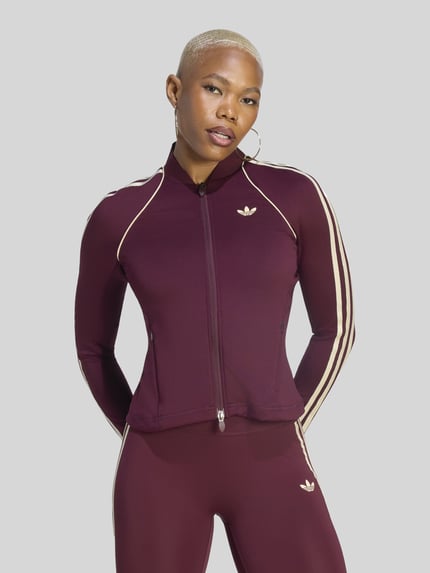 Frauenmodel trägt Slim Fit Trainingsjacke mit Logo-Detail von adidas, Farbe Bordeaux mit weißen Streifen, glatte Textur, adidas Training, Nahaufnahme Oberkörper.