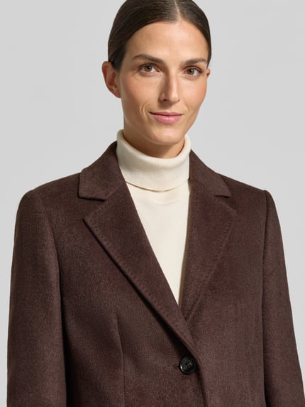Kobiece model prezentuje krótki płaszcz z Pattentaschen von JAKE*S WOMAN COLLECTION, jednokolorowy, krój regular fit, detal z logo, szwy działowe, długi rękaw, kołnierz z połami, zapięcie na 2 guziki, rozporek, zaszewki, materiał o gładkiej fakturze, nahaufnahme oberkörper.