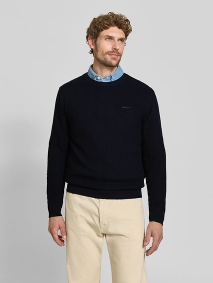 Männermodel trägt Regular Fit Pullover aus Baumwoll-Woll-Mix von GANT in Dunkelblau, helle Hose, Ganzkörperansicht von vorne.