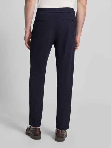 Mężczyzna nosi Relaxed Fit Sweatpants mit Viskose-Anteil von Lindbergh, elastyczna mieszanka materiałów z dodatkiem wiskozy, kanty, krój relaxed fit, tunel, szerokość w rozmiarze M: 41 cm, długość wewnętrzna nogawki w rozmiarze M: 79 cm, ciemnogranatowe, gładka tekstura, widok całej sylwetki od tyłu